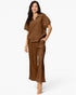 A woman modeling a matching brown lounge set consisting of a short-sleeve half-zip pullover and wide-leg pants, photographed against a clean white studio background.