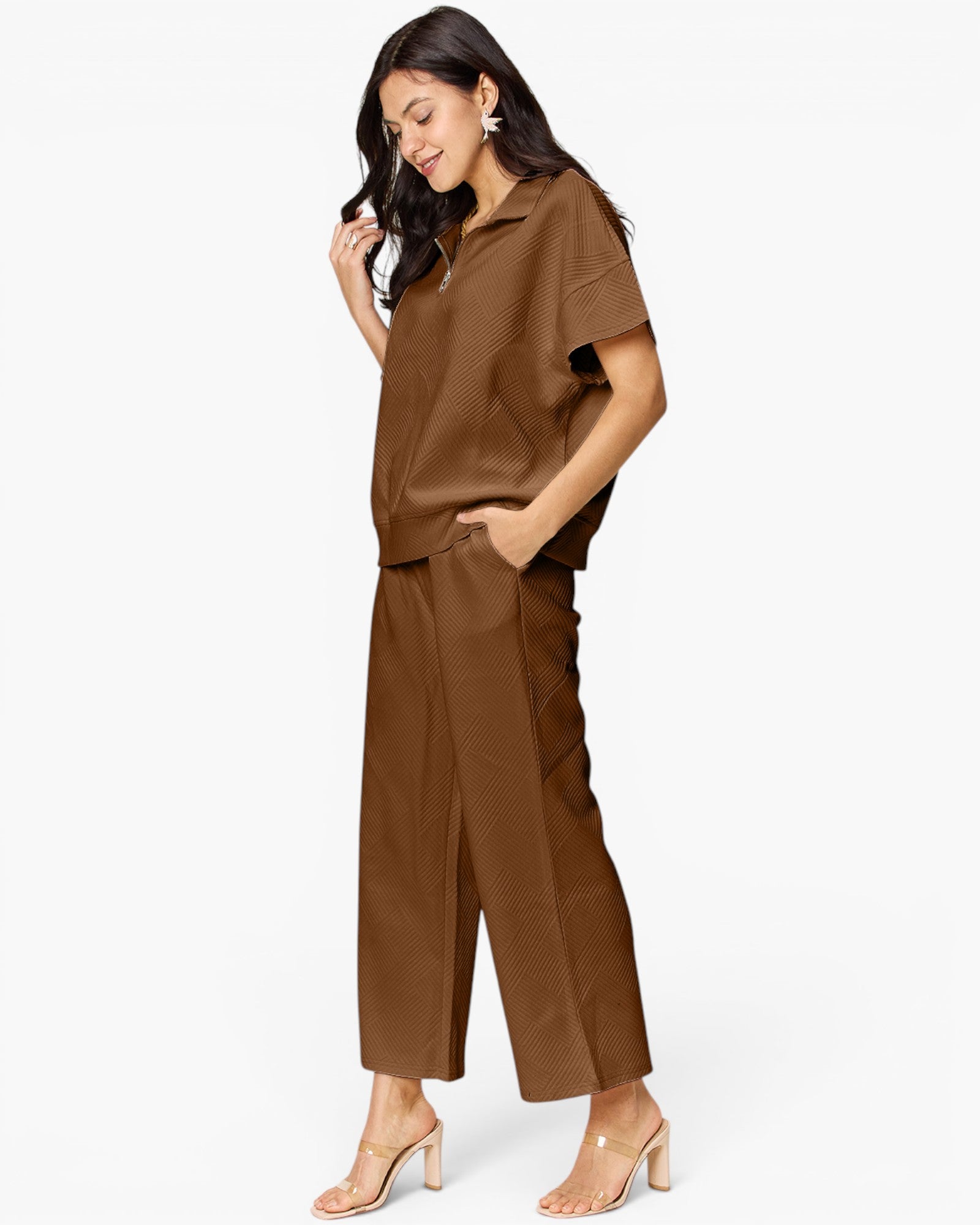 A woman modeling a matching brown short-sleeve collared top and wide-leg cropped pants set, paired with clear-strap heeled sandals, against a plain white studio background.