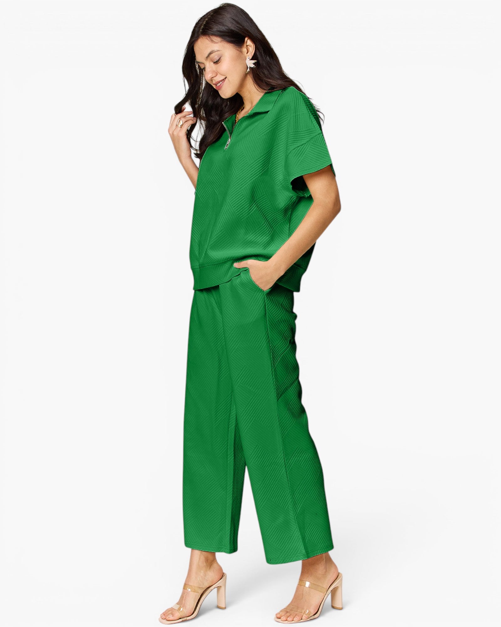 A woman modeling a bright green matching two-piece set consisting of a short-sleeve collared top and wide-leg cropped pants, paired with clear-strap heeled sandals against a plain white studio background.