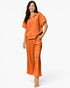 A woman modeling a matching two-piece lounge set in a vibrant orange color, featuring a short-sleeve half-zip top and wide-leg pants, set against a plain white studio background.
