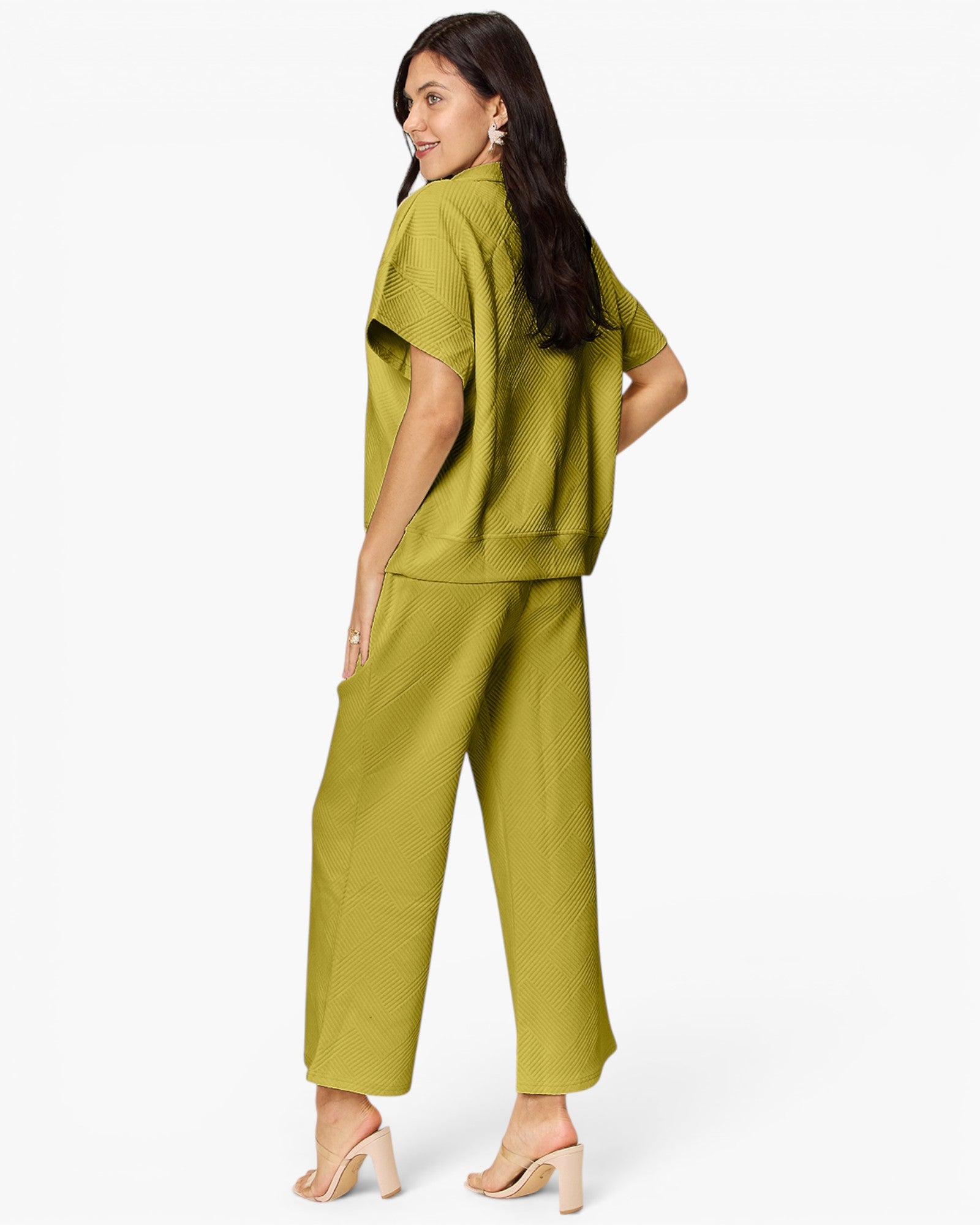 A woman modeling a matching two-piece olive green set consisting of a short-sleeve cropped top and wide-leg cropped pants, shown from a three-quarters back view against a plain white studio background.