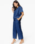 A woman modeling a matching navy blue two-piece set consisting of a short-sleeve collared top and wide-leg cropped pants, paired with clear-strap heeled sandals against a plain white studio background.