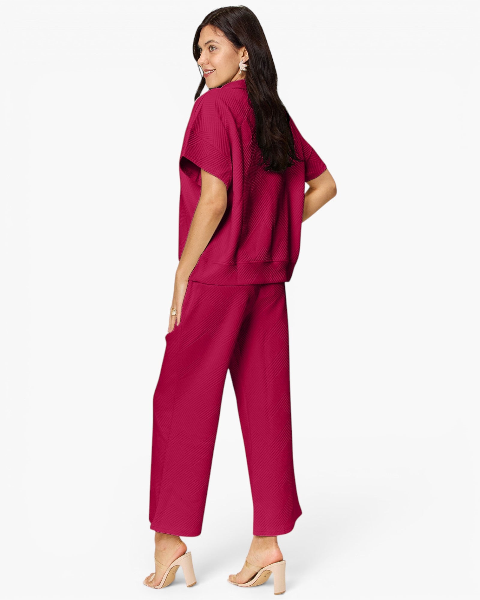 A woman modeling a matching magenta two-piece lounge set consisting of a short-sleeve top and wide-leg cropped pants, shown from a three-quarters back view against a plain white studio background.