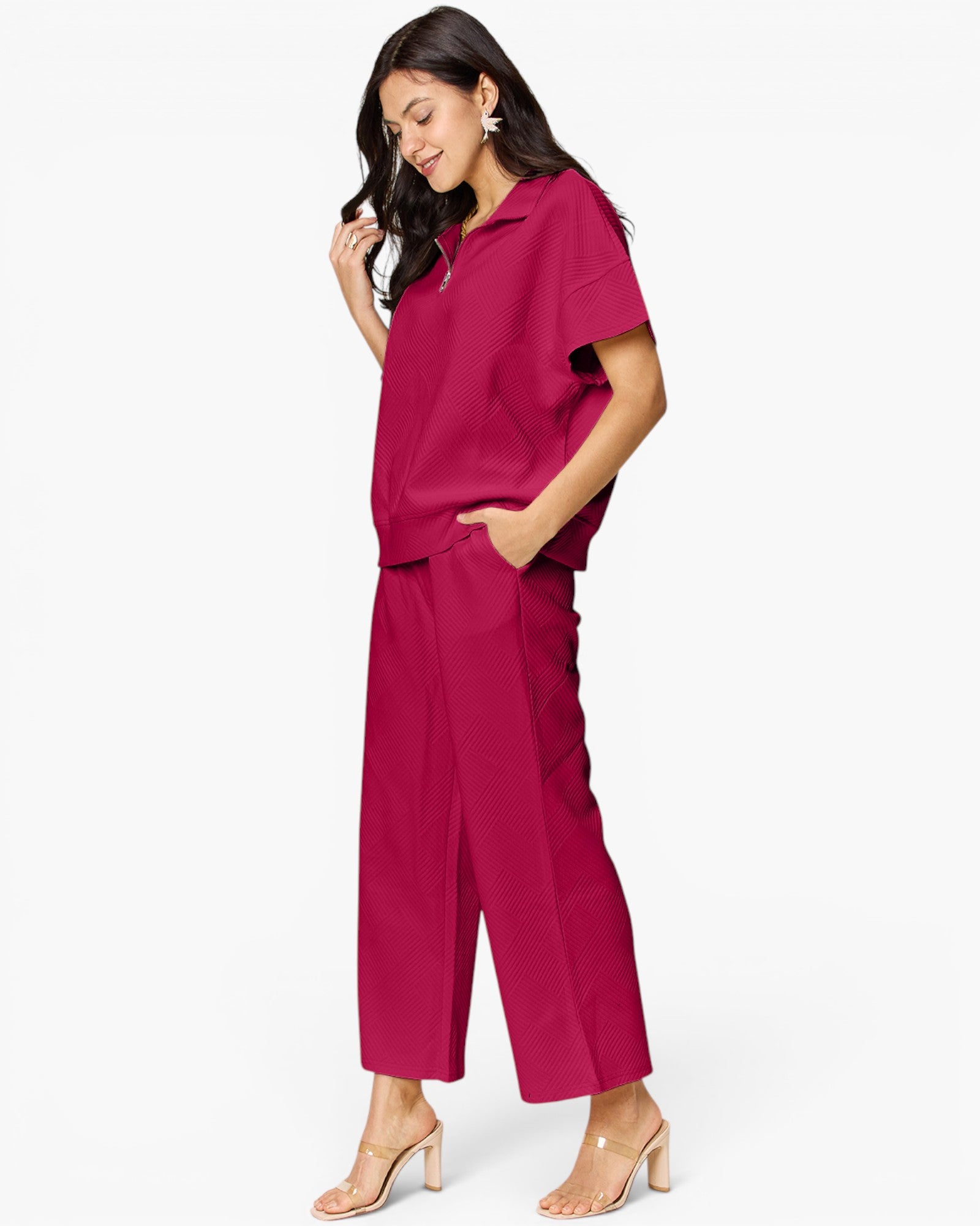 A woman modeling a matching magenta two-piece set consisting of a short-sleeve collared top and wide-leg cropped pants, paired with clear-strap heeled sandals against a plain white background.