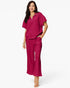 A woman modeling a matching magenta two-piece lounge set consisting of a short-sleeve half-zip top and wide-leg pants, shot against a plain white studio background.