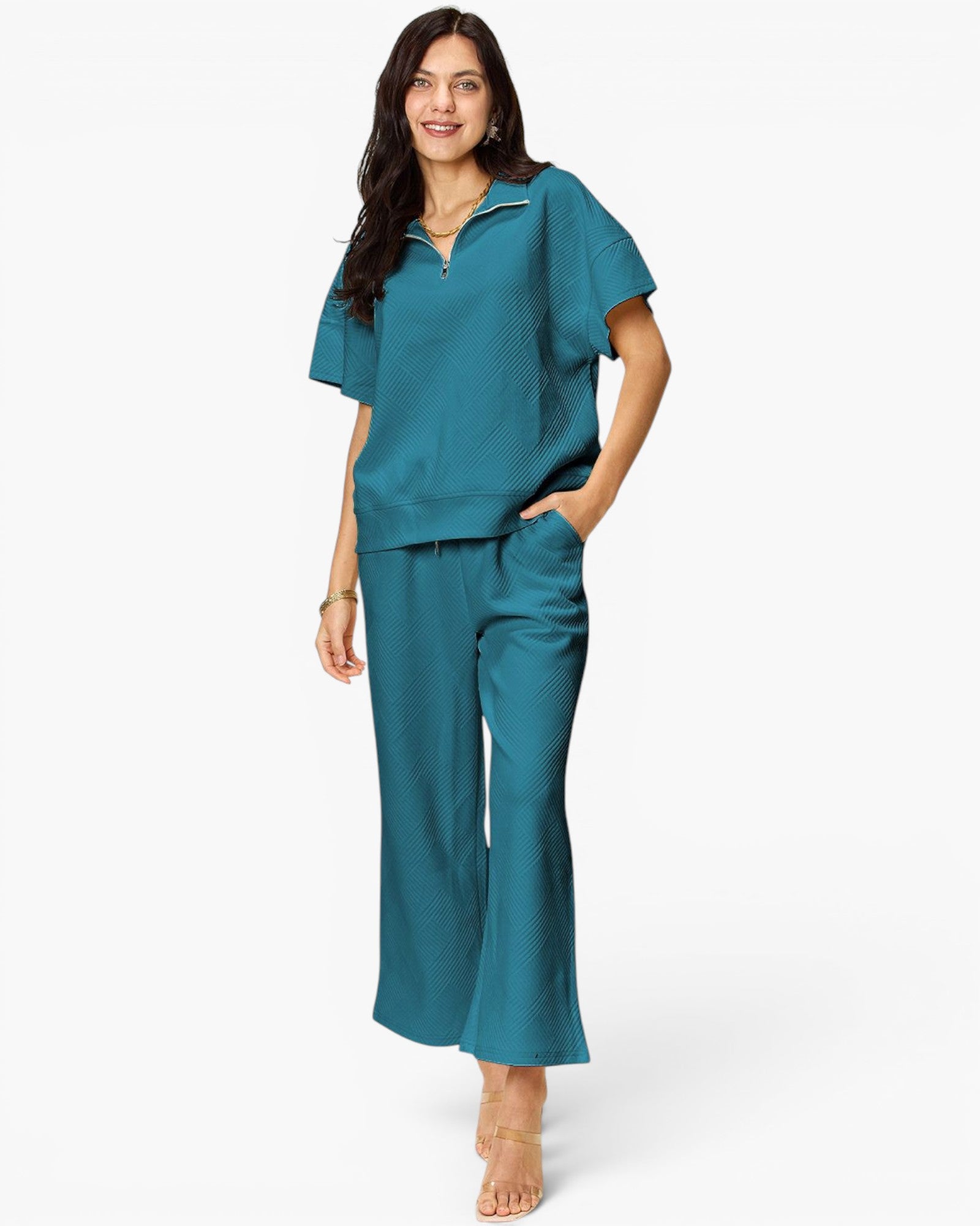 A woman modeling a matching teal two-piece lounge set consisting of a short-sleeve half-zip top and wide-leg pants, photographed against a clean white studio background.