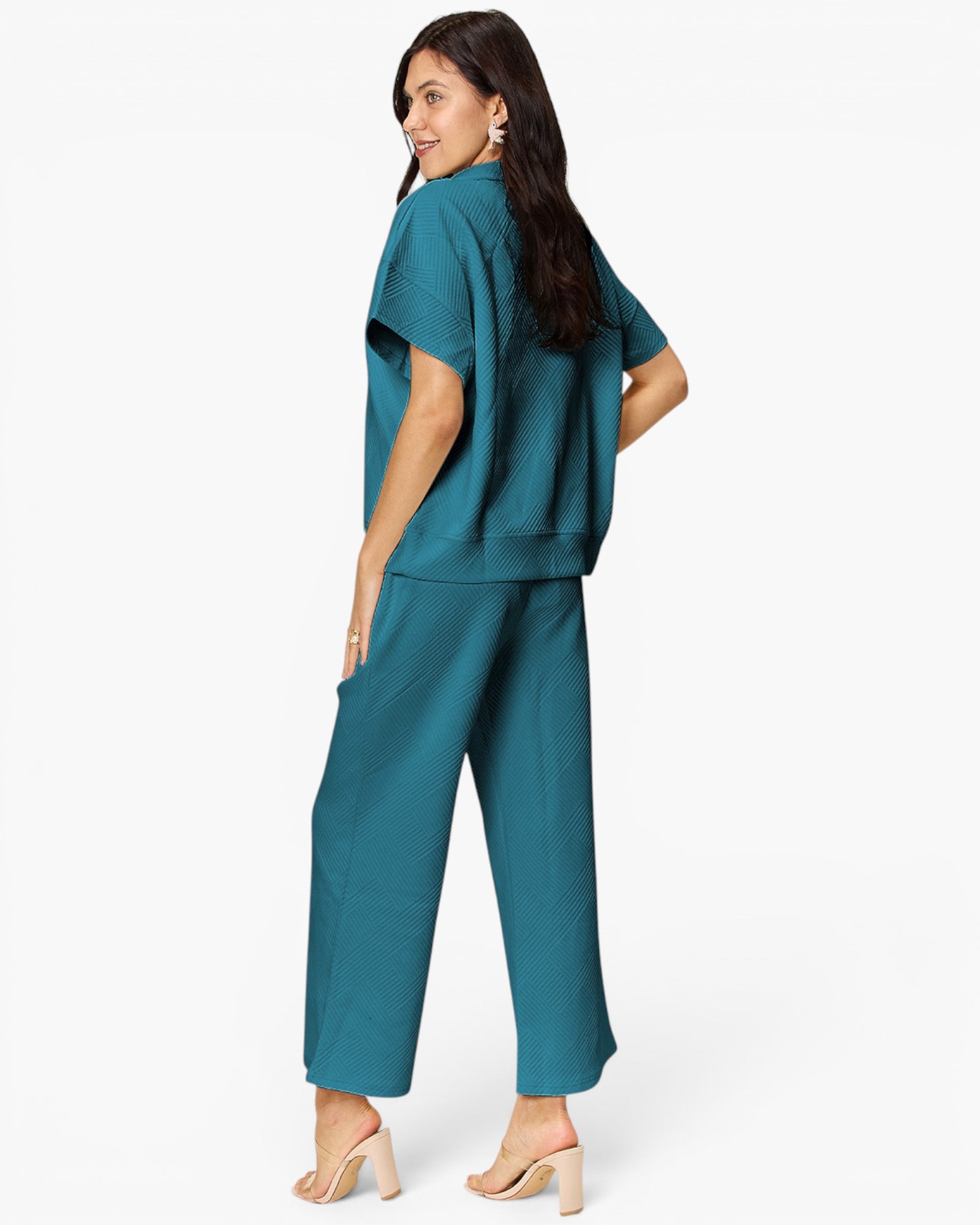 A woman modeling a teal two-piece lounge set consisting of a short-sleeve top and matching wide-leg pants, shown from a three-quarters back view against a plain white studio background.