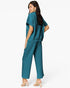 A woman modeling a teal two-piece lounge set consisting of a short-sleeve top and matching wide-leg pants, shown from a three-quarters back view against a plain white studio background.