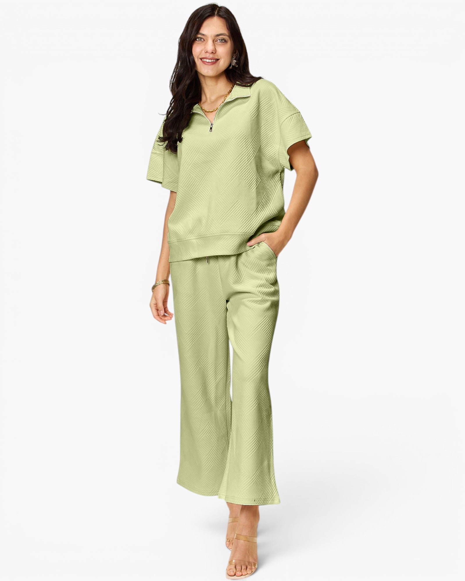 A woman modeling a light sage green two-piece loungewear set consisting of a short-sleeve collared top and matching wide-leg cropped pants, set against a plain white studio background.
