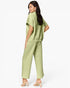 A woman modeling a light sage green two-piece set consisting of a short-sleeve cropped top and matching wide-leg cropped pants, shown from a three-quarters back view against a plain white studio background.