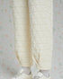 Quilted cream-colored pants worn with white sneakers on a light floral-patterned background