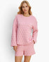 A woman modeling a light pink two-piece quilted loungewear set consisting of a long-sleeve top and matching shorts, set against a plain white studio background.