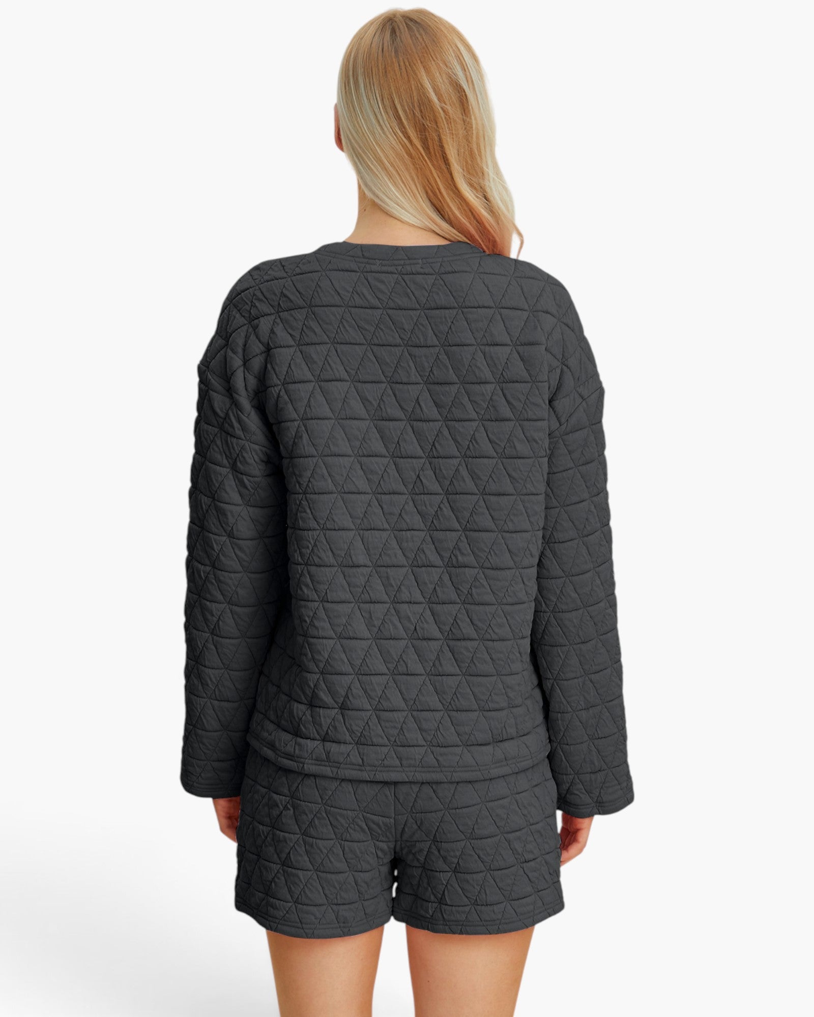 A woman viewed from the back wearing a dark gray quilted long-sleeve top and matching shorts against a plain white studio background.