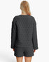 A woman viewed from the back wearing a dark gray quilted long-sleeve top and matching shorts against a plain white studio background.