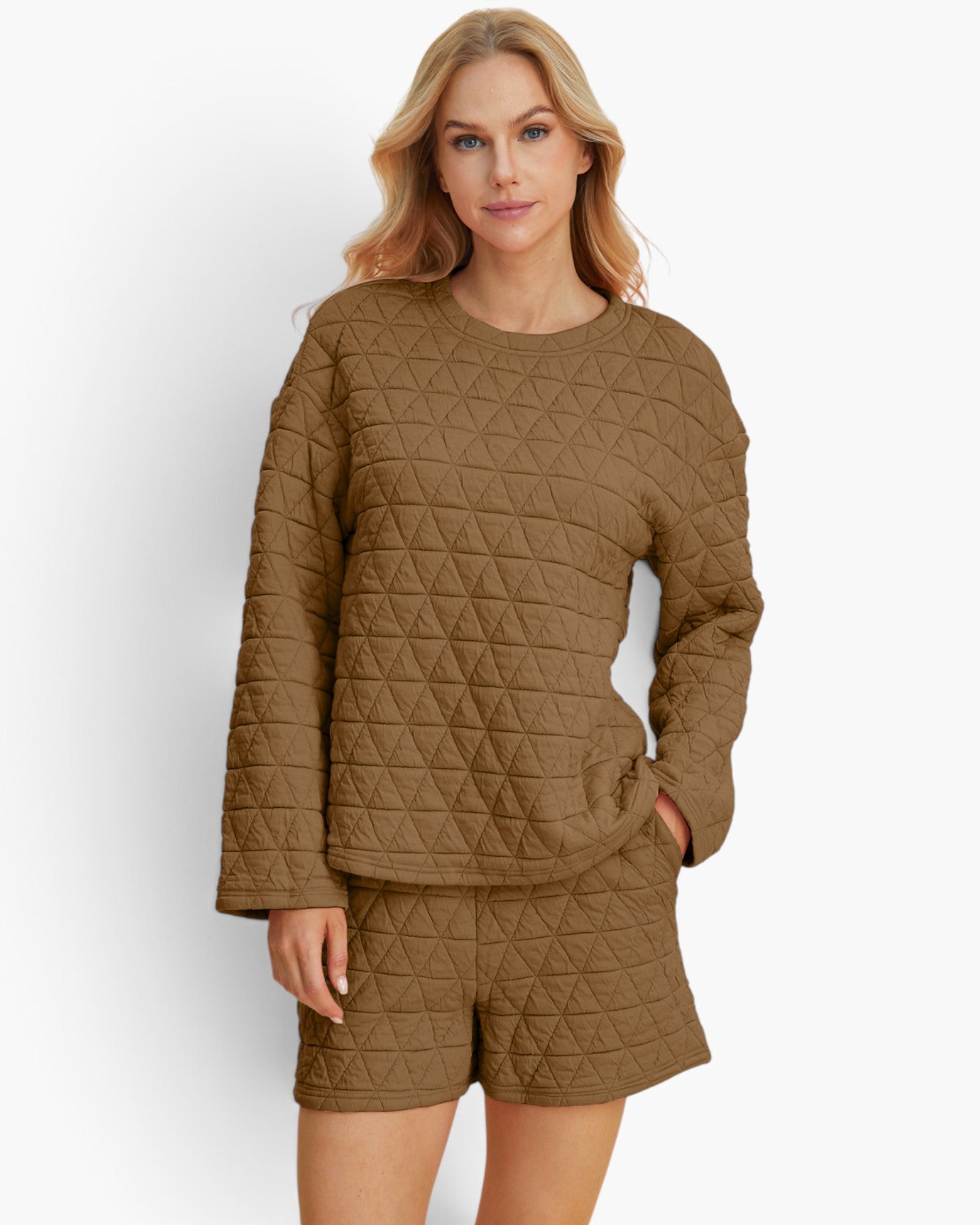 A woman modeling a matching quilted lounge set consisting of a long-sleeve top and shorts in a warm brown color, set against a plain light gray background.
