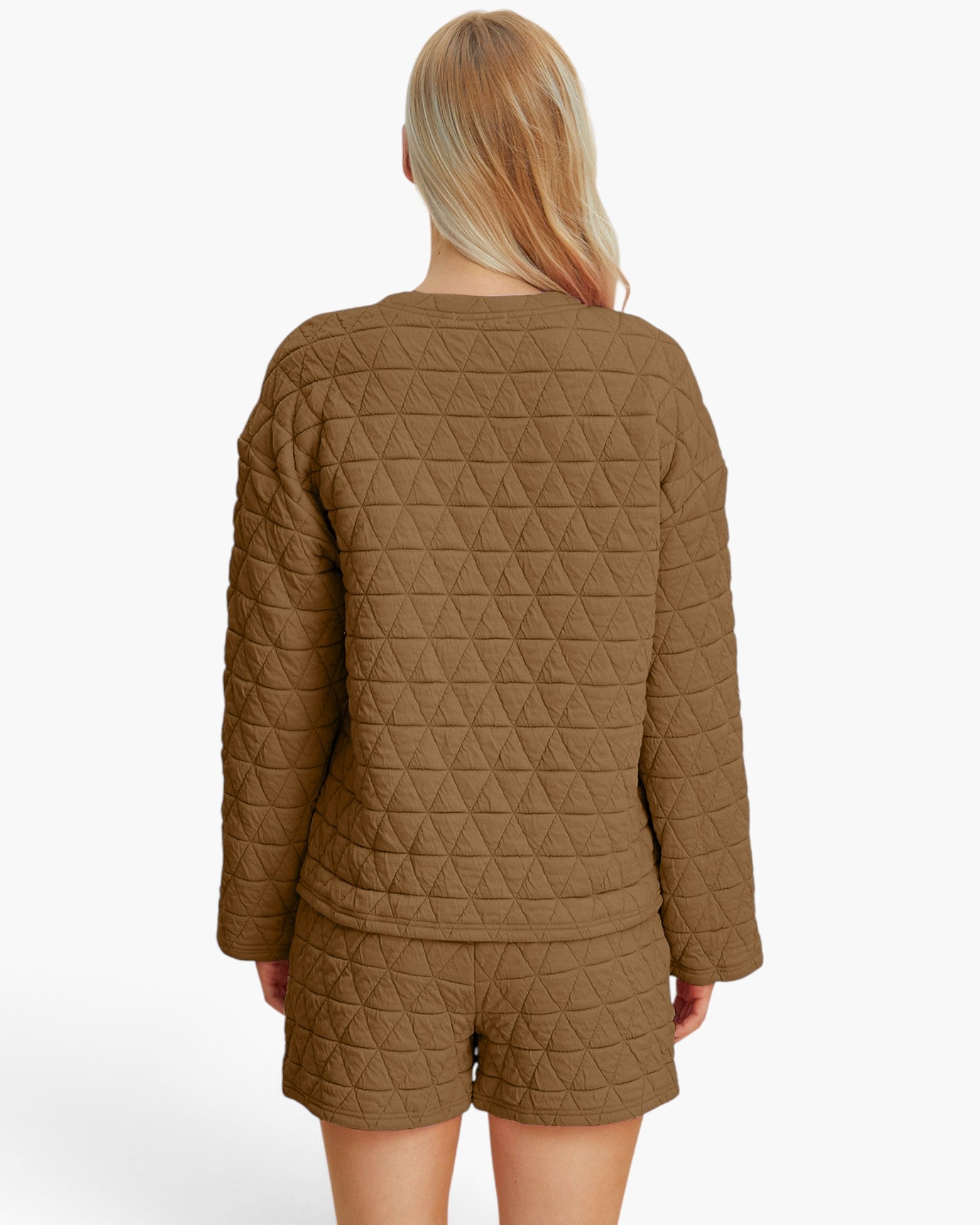 A woman viewed from the back wearing a matching quilted lounge set in a warm camel brown color, featuring a long-sleeve top and shorts, against a plain white studio background.