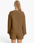 A woman viewed from the back wearing a matching quilted lounge set in a warm camel brown color, featuring a long-sleeve top and shorts, against a plain white studio background.