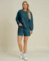 Woman wearing a teal sweatshirt and shorts set on a beige background