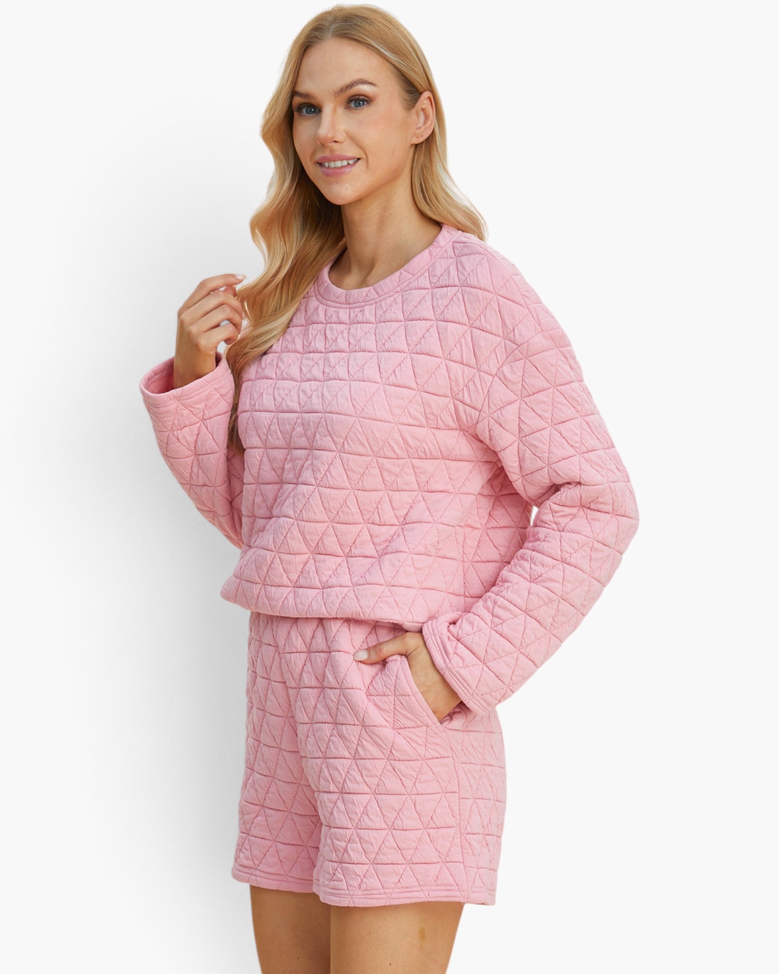 A woman modeling a light pink quilted two-piece loungewear set consisting of a long-sleeve top and matching shorts, set against a plain white studio background.