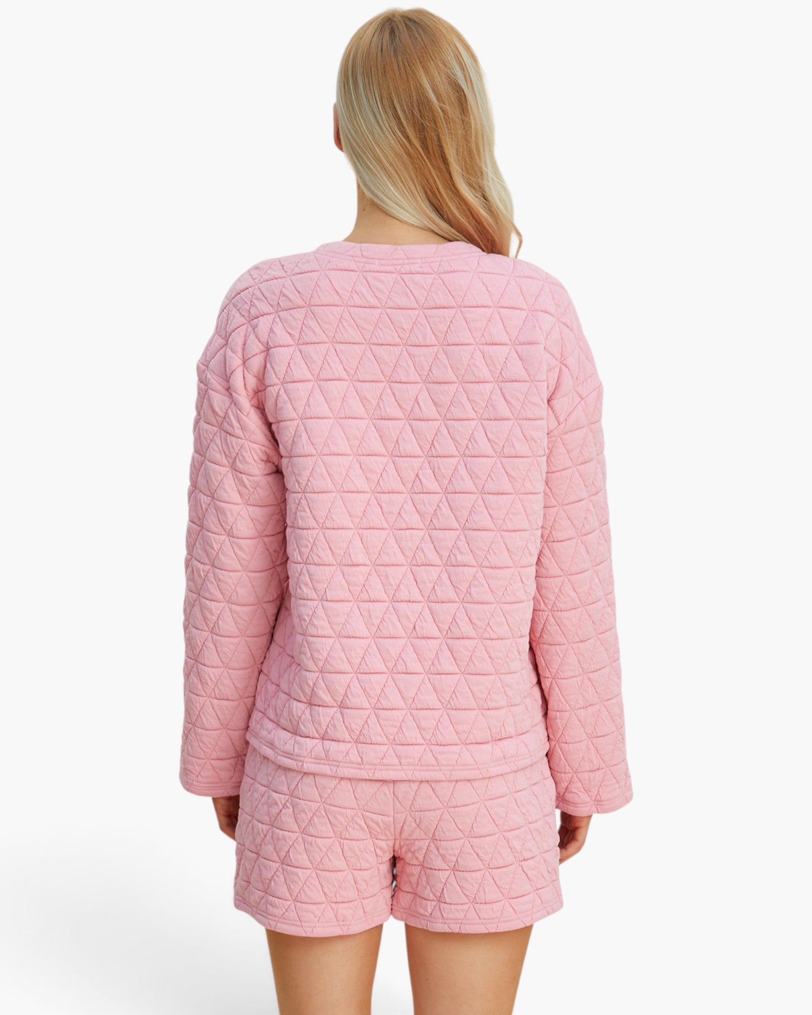 A woman shown from the back wearing a light pink quilted two-piece pajama set with a long-sleeve top and matching shorts against a plain white background.