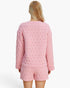 A woman shown from the back wearing a light pink quilted two-piece pajama set with a long-sleeve top and matching shorts against a plain white background.