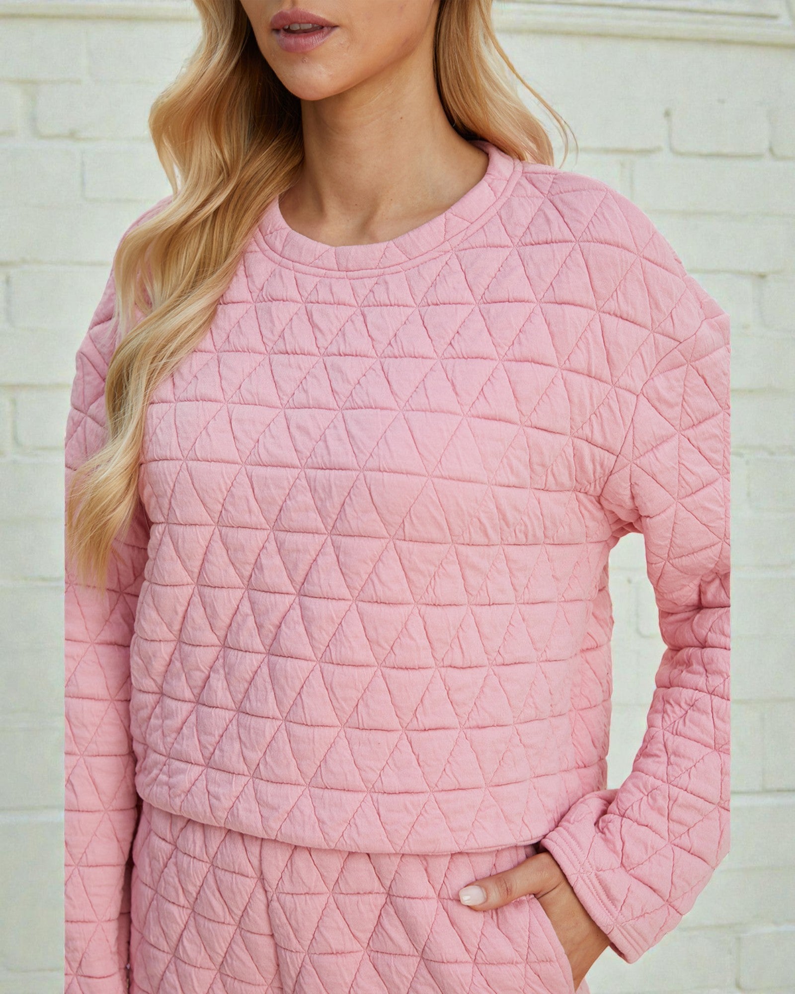 Person wearing a pink quilted sweater against a white brick wall