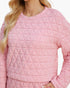 A close-up of a woman wearing a light pink quilted long-sleeve top with a geometric diamond pattern, set against a plain white background.