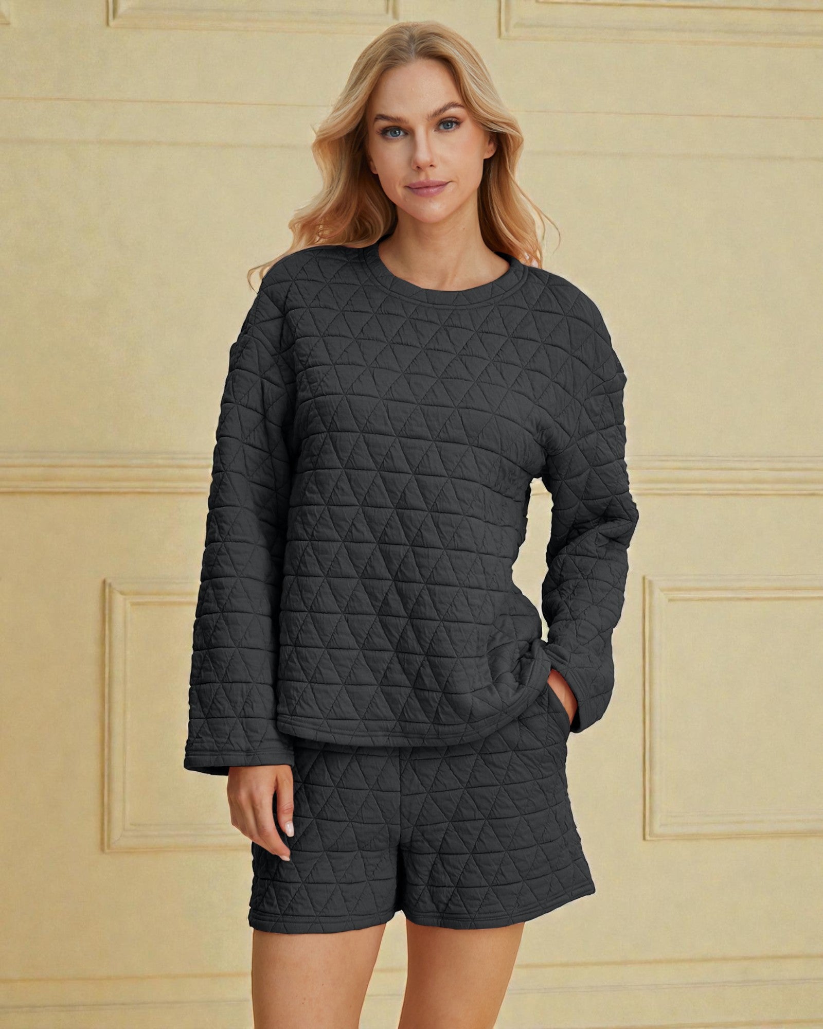 Woman wearing a dark gray quilted sweater and shorts set against a beige wall.
