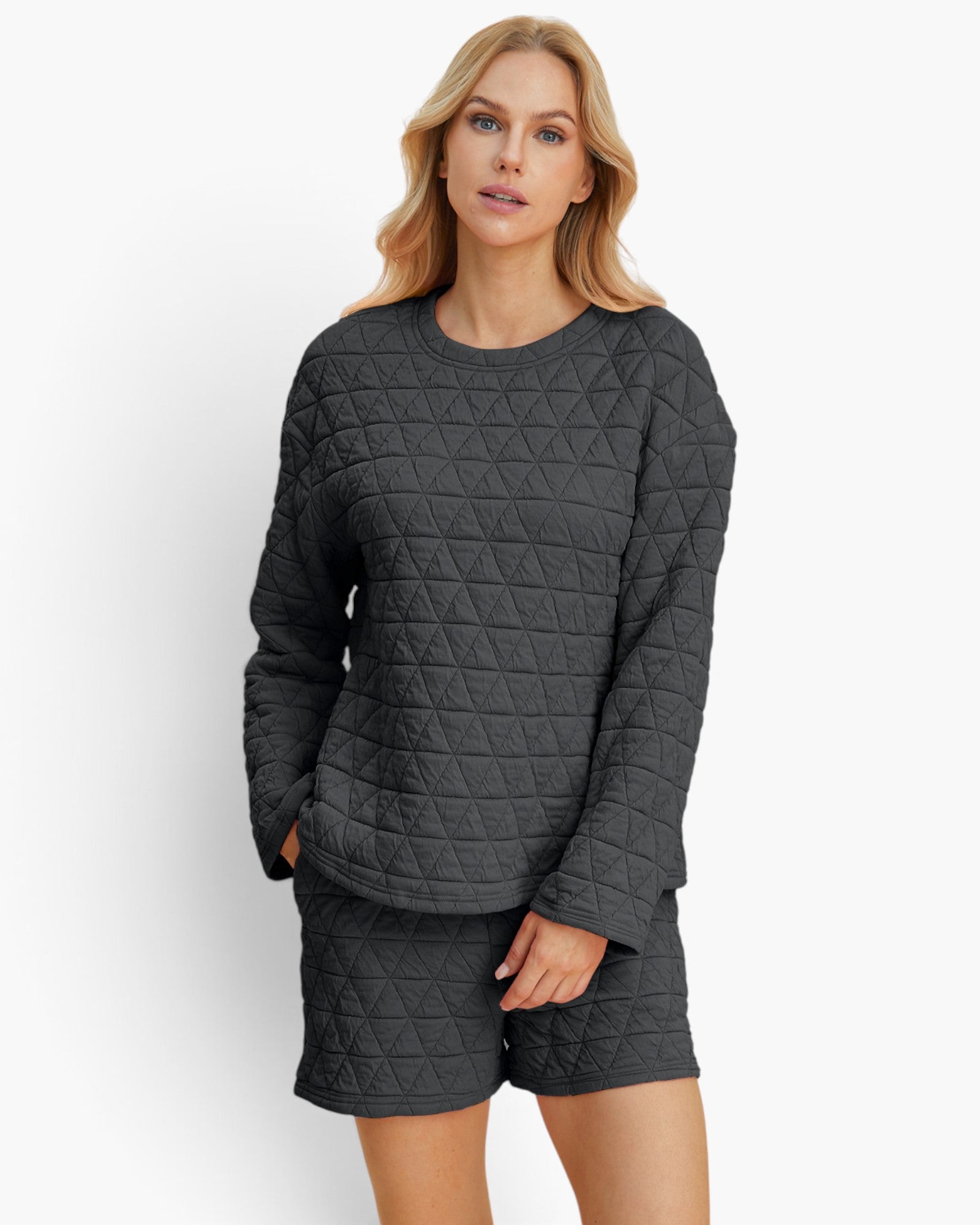 A woman modeling a dark gray quilted two-piece lounge set consisting of a long-sleeve top and matching shorts, shot against a plain white studio background.