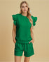 Woman wearing a green outfit with ruffled sleeves against a beige background