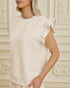 Woman wearing a beige top with ruffled sleeves against an ornate wall.