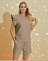Woman wearing a beige outfit with ruffled sleeves against a beige background