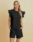 Woman wearing a black outfit with ruffled sleeves on a beige background