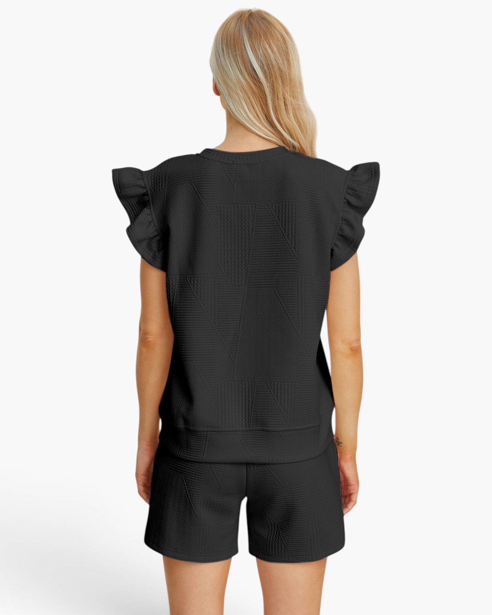 A woman shown from the back wearing a black textured short-sleeve top with ruffled shoulders and matching black shorts against a plain white studio background.