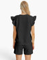 A woman shown from the back wearing a black textured short-sleeve top with ruffled shoulders and matching black shorts against a plain white studio background.