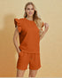 Woman wearing an orange outfit with ruffled sleeves against a beige background