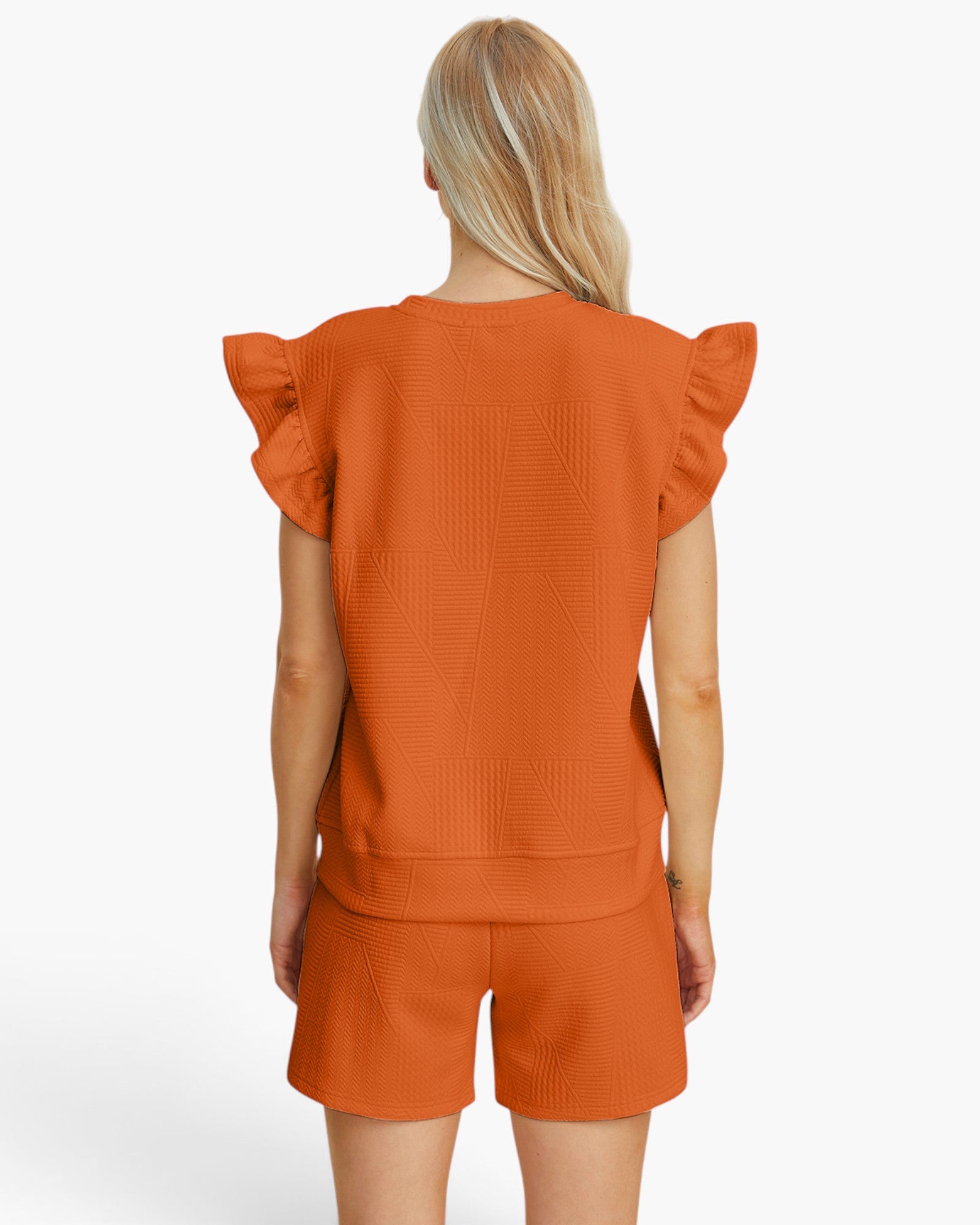 A woman shown from the back wearing a matching burnt orange textured knit set consisting of a short-sleeve top with ruffled shoulders and matching shorts, against a plain white studio background.