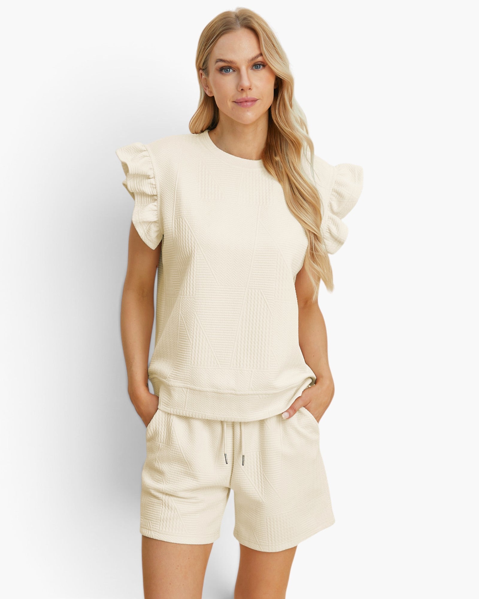 A woman modeling a cream-colored two-piece lounge set consisting of a textured short-sleeve top with ruffled shoulders and matching drawstring shorts, set against a plain light gray studio background.