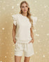 Woman wearing a white outfit with ruffled sleeves against a gold background