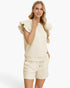 A woman modeling a matching cream-colored lounge set consisting of a textured short-sleeve top with ruffled shoulders and matching drawstring shorts, set against a plain white studio background.