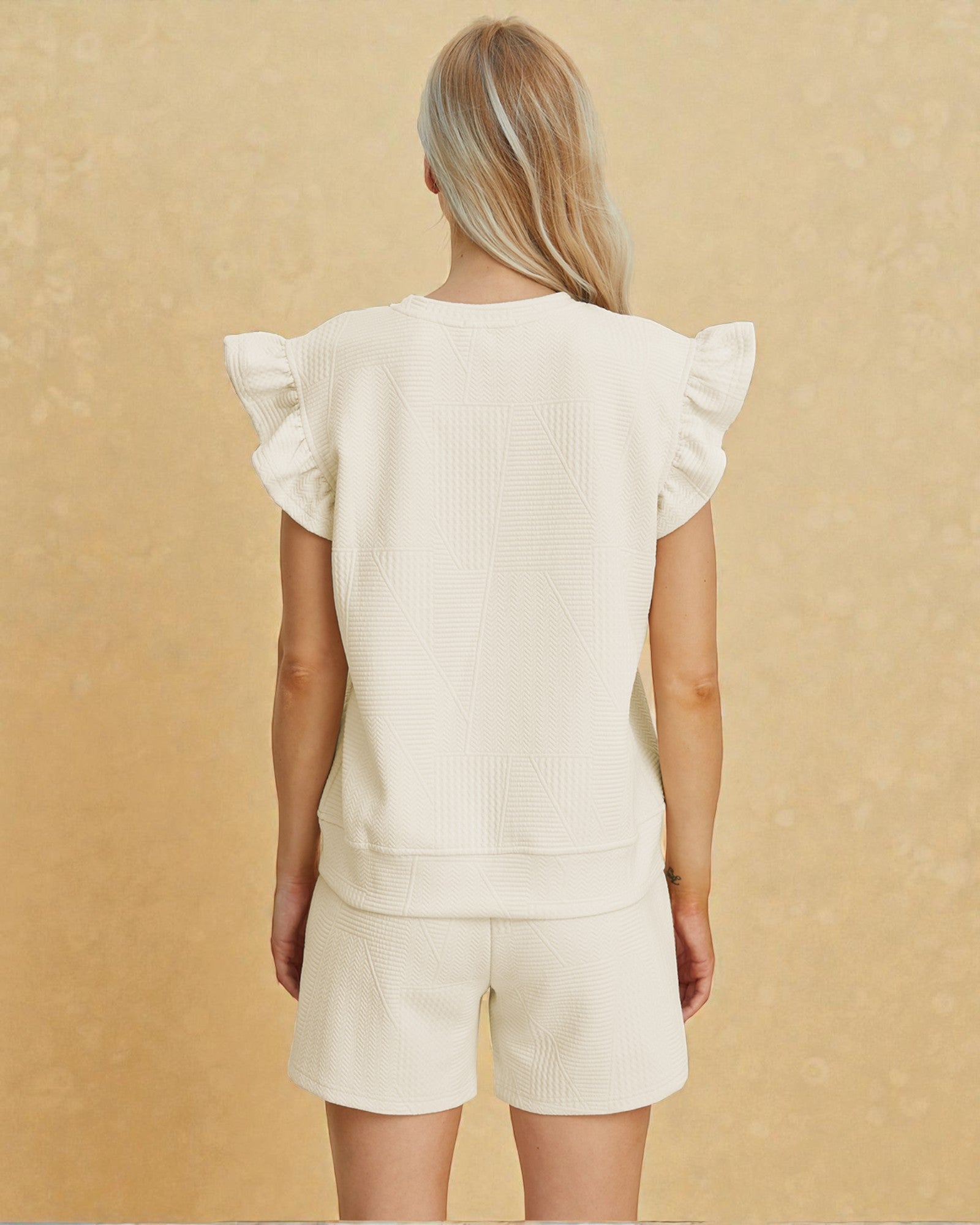 Person wearing a cream-colored outfit with ruffled sleeves on a beige background