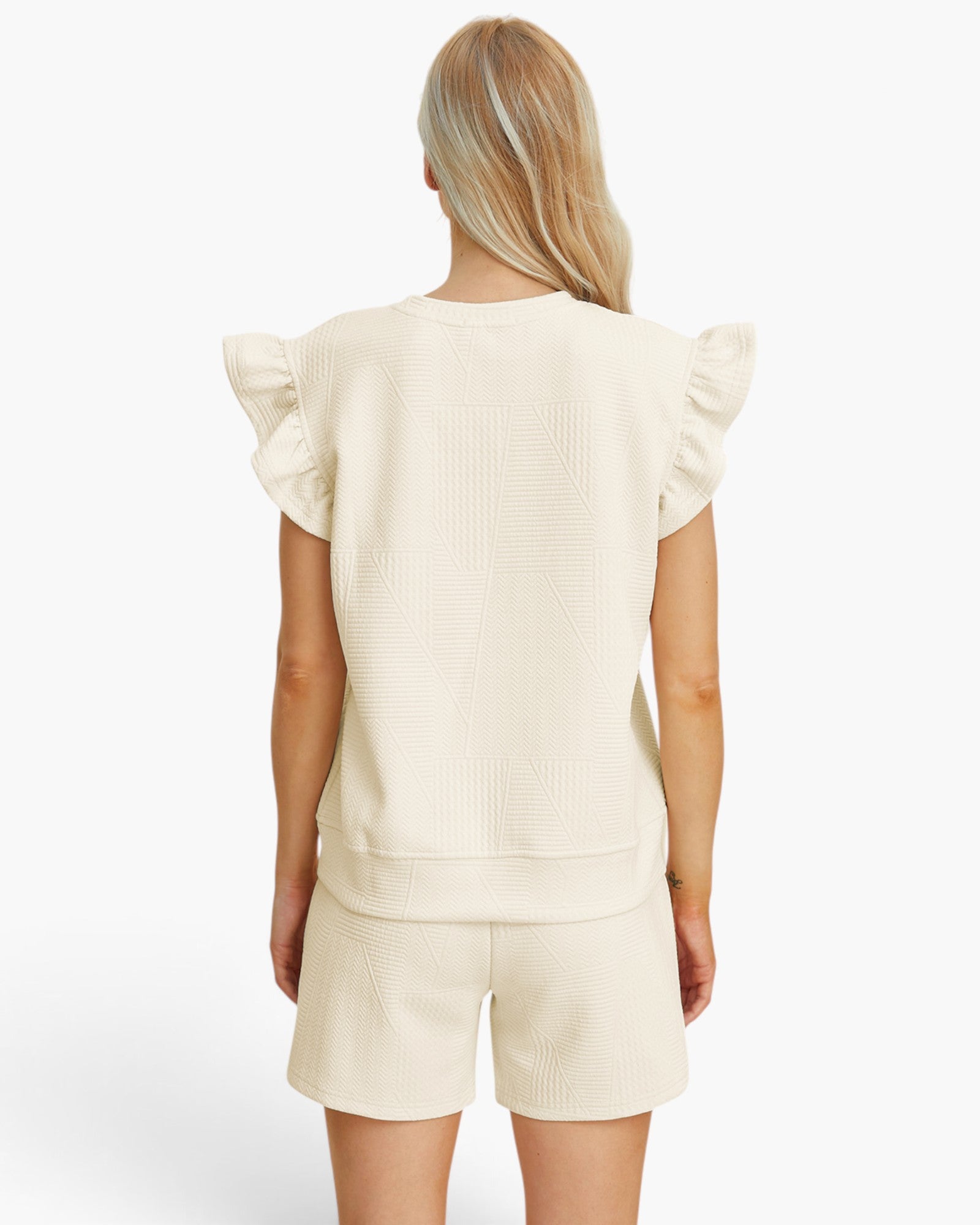 A woman shown from the back wearing a cream-colored textured short-sleeve top with ruffled shoulders and matching textured shorts against a plain white studio background.