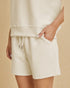 Person wearing a textured beige outfit with shorts and a top on a beige background