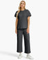 A woman modeling a dark gray quilted matching set consisting of a short-sleeve top and cropped wide-leg pants, paired with white sneakers against a light gray studio background.
