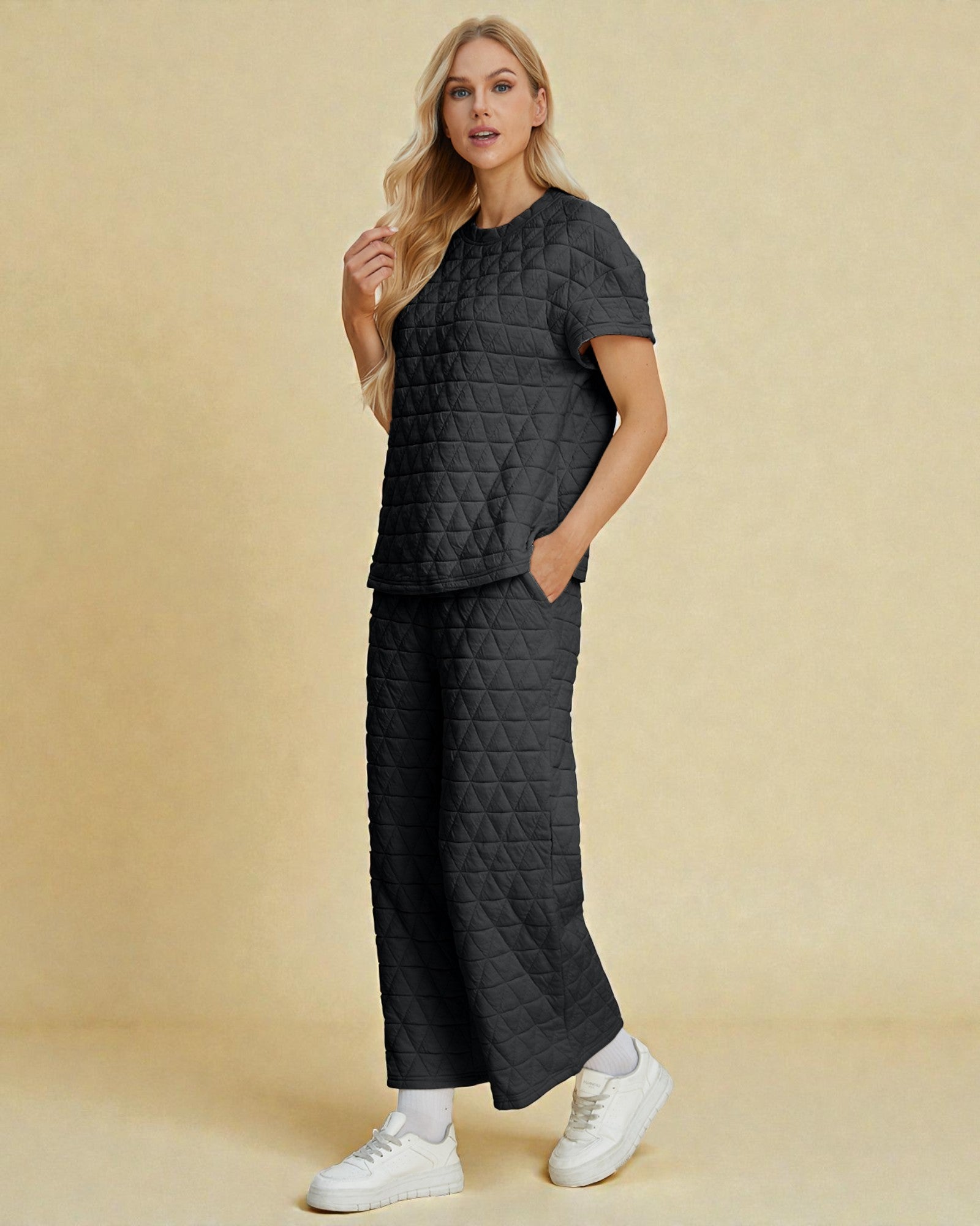 Woman wearing a black quilted outfit with white sneakers on a beige background