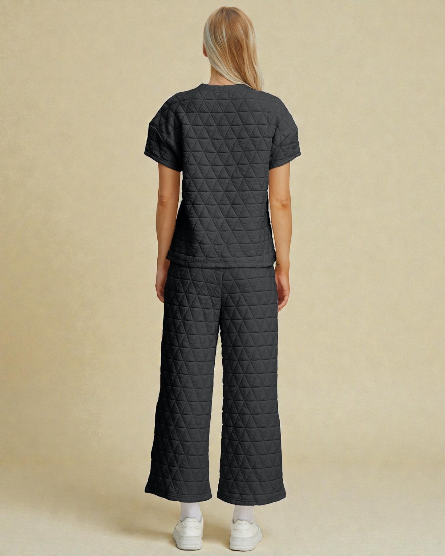 Person wearing a dark gray quilted outfit on a beige background