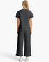 A woman shown from the back wearing a dark gray quilted short-sleeve top and matching wide-leg pants, paired with white sneakers, against a light gray studio background.