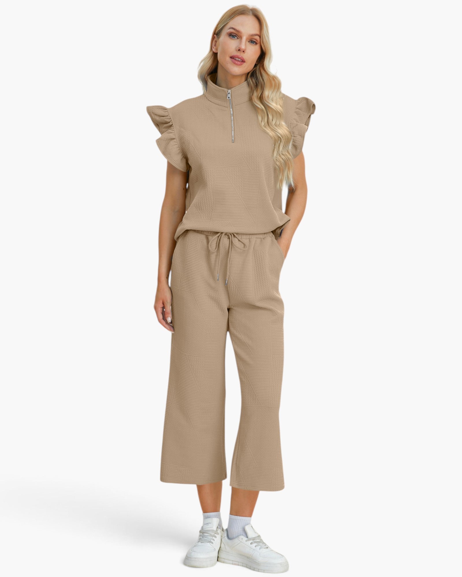 A woman modeling a matching beige two-piece set consisting of a short-sleeve mock-neck top with ruffled shoulders and a drawstring waist, paired with matching wide-leg cropped pants, against a plain light background.
