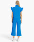 A model viewed from the back wearing a bright blue matching set consisting of a short-sleeve top with ruffled shoulders and high collar, paired with matching wide-leg cropped pants, on a light gray studio background.
