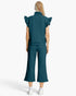 A model viewed from the back wearing a matching dark teal ribbed two-piece set consisting of a short-sleeve top with ruffled shoulders and wide-leg cropped pants, paired with white sneakers on a light gray background.